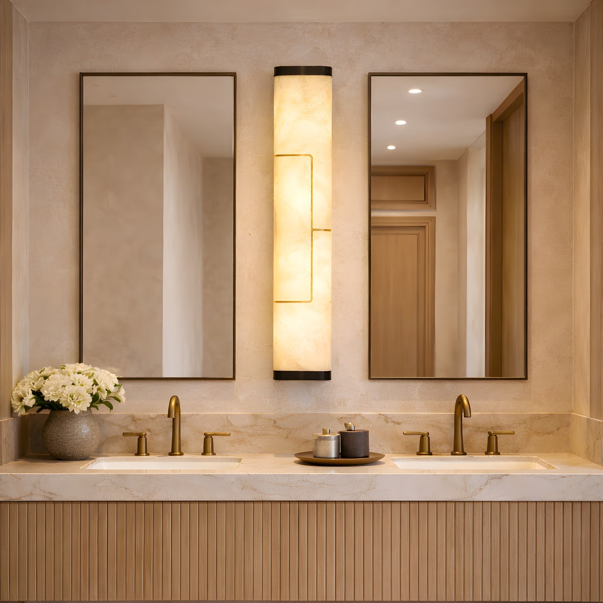 Elegant bathroom with double sinks, two rectangular mirrors, the Eryndor LED Alabaster Wall Light in matte black & soft white, gold fixtures, and white flowers on a marble countertop. Warm, neutral tones complete the space.