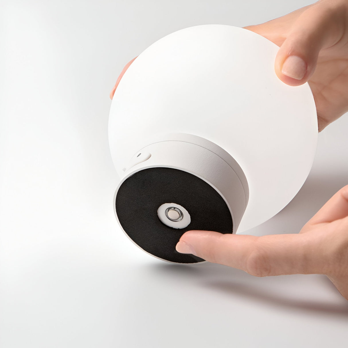 Close-up of a hand adjusting the Beam Outdoor Table Lamp in White, featuring a sleek circular design with a white top and black base. The person is pressing a button on the minimalist underside, all set against a simple white background.