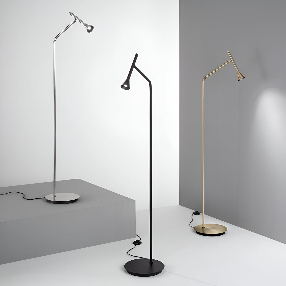 The Solenia LED Floor Lamp 4.5W 3000K in black is showcased alongside two other versions, each featuring a sleek and modern design with finishes in silver and gold. Set against a minimalist gray backdrop, these lamps boast slender profiles with round bases and angled heads, providing energy-efficient illumination that enhances any contemporary setting.