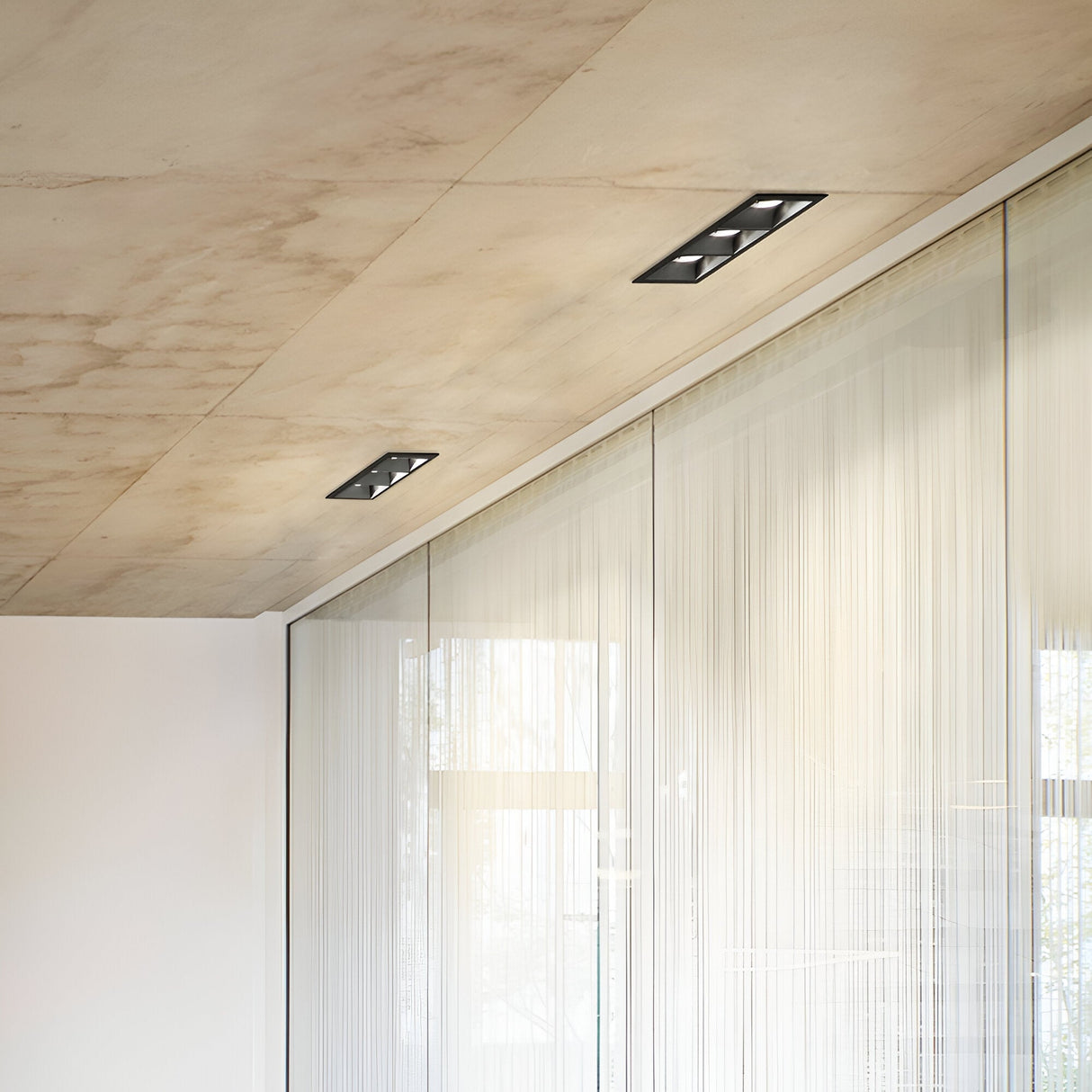 A modern interior with a ceiling featuring Voltis Square Triple Frame 206mm lights in a sleek black finish. The room's large glass walls, adorned with sheer curtains, allow natural light to filter through, complementing the minimalist design of the ceiling and walls.