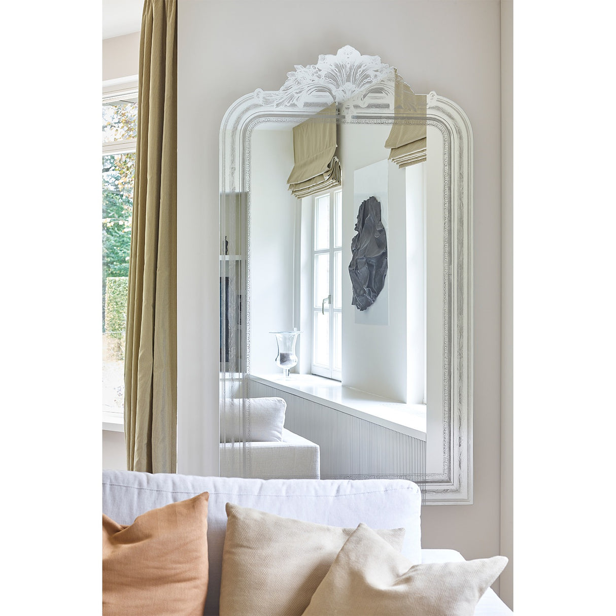 Haussmann full length mirror with scrolled crest and moulded frame, reflecting a light neutral living room with curtains, artwork, and a sofa with cushions.