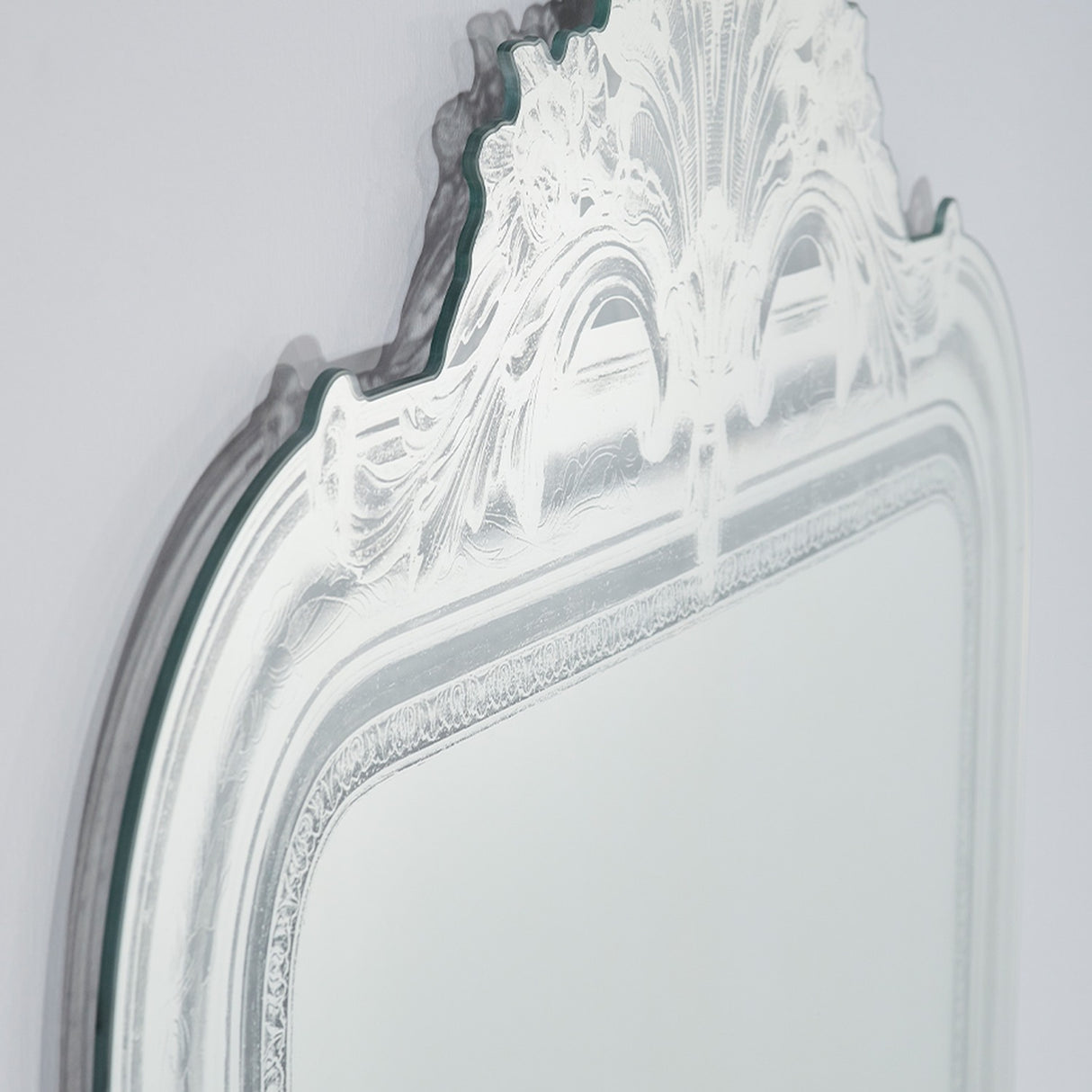 Close-up of the Haussmann full length mirror's scrolled crest and etched glass border, showing the moulded frameless design against a plain light background.