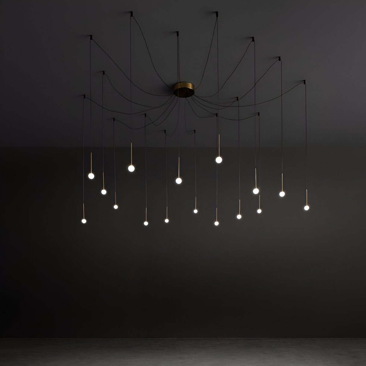 Introducing the Nimbus 16 LED Light Suspension, a luxurious modern chandelier with multiple thin black wires elegantly extending from a central ceiling fixture, each capped with a small glowing bulb. The brass finish beautifully accentuates its simplicity and elegance against the dark backdrop.