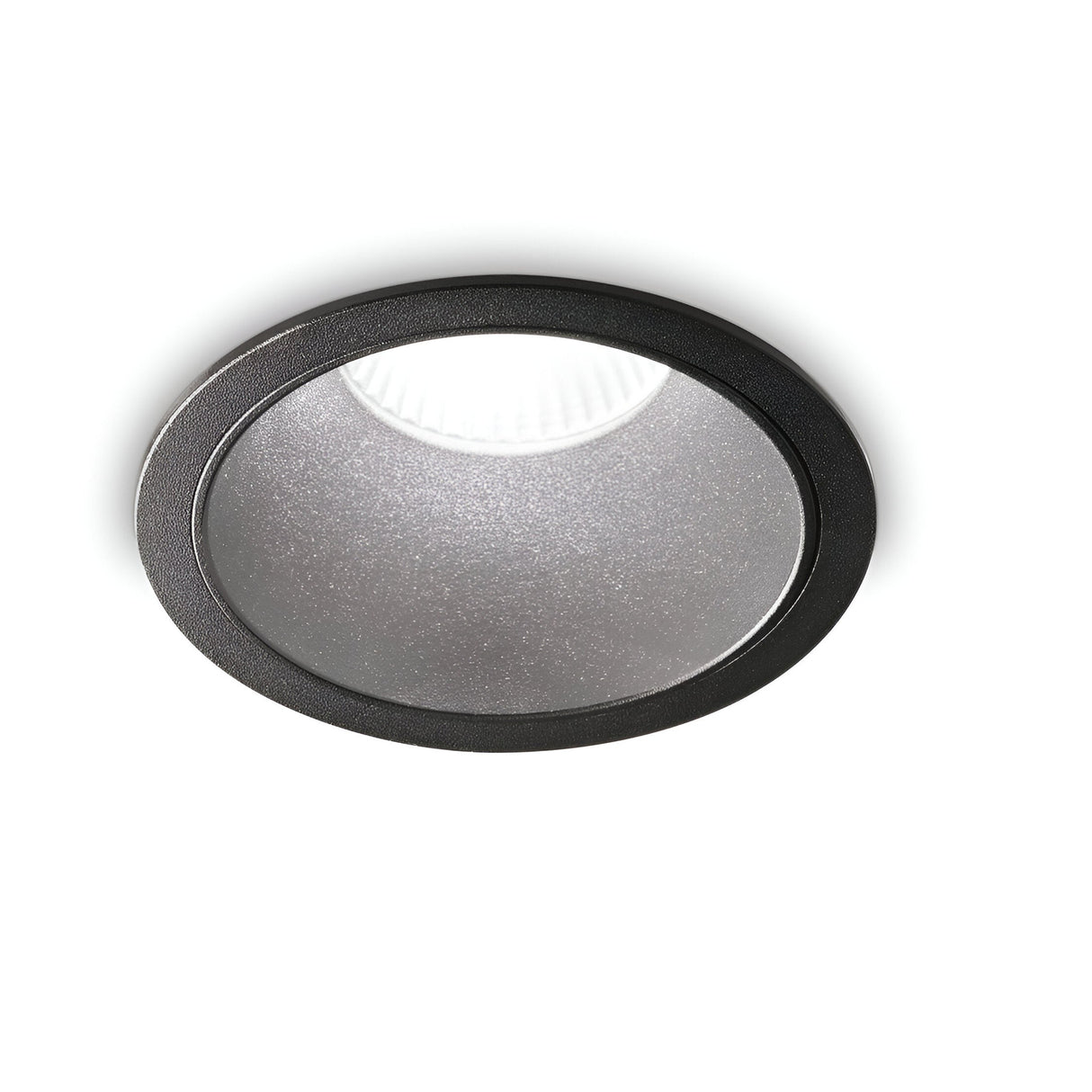 The Sally LED Round Recessed Trim Downlight - 11W, 2700K, Black illuminates with a bright white glow and is framed by its sleek black trim, making it an energy-efficient lighting solution against a minimalist white backdrop.