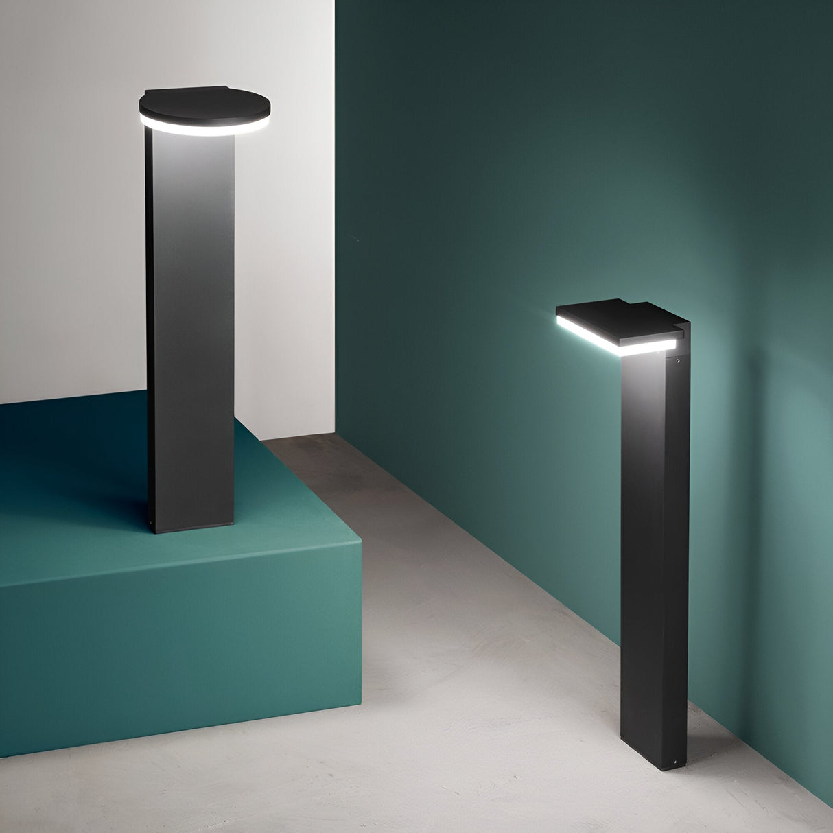 Two sleek, contemporary floor lamps featuring minimalist designs and energy-efficient LED lighting. One is circular on a pedestal and the other is angled, placed against a teal and gray backdrop. Illuminate your modern space with the warm glow of 3000K light from the Arcetra Square Outdoor LED Bollard Light in Grey.