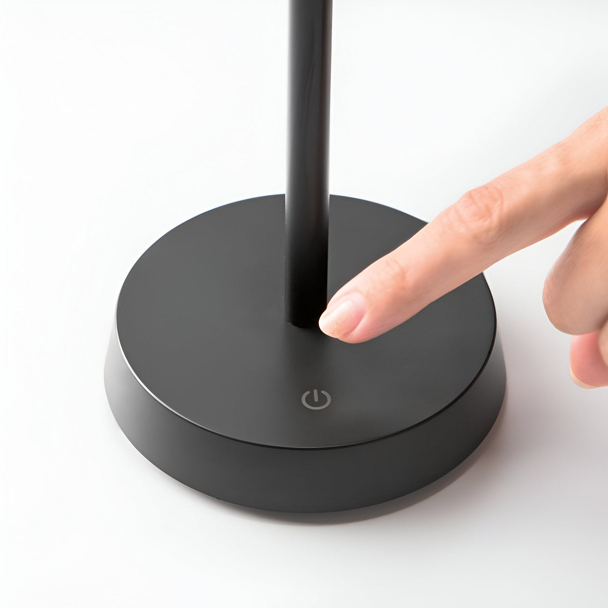 A close-up of a person pressing the power button on the base of a Solitus LED Outdoor Table Lamp 2.8W 3000K - Black with a minimalist design. The lamp boasts an IP54 rating for enhanced durability against the elements. The background is a smooth white surface.