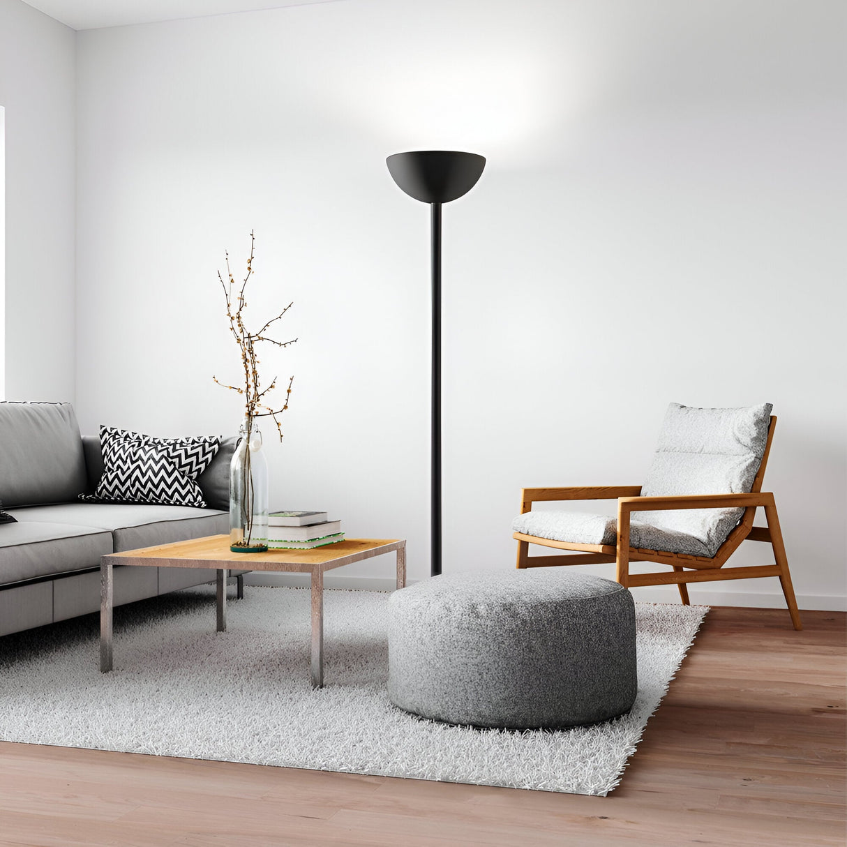 A modern living room showcases a gray sofa adorned with patterned pillows, a wooden armchair with a cushion, and a round gray ottoman atop a fluffy rug. A sleek floor lamp and the Arion-1 Large Ceiling Lampshade in Rose Black amplify the modern elegance, while a glass vase filled with branches rests on the wooden coffee table.