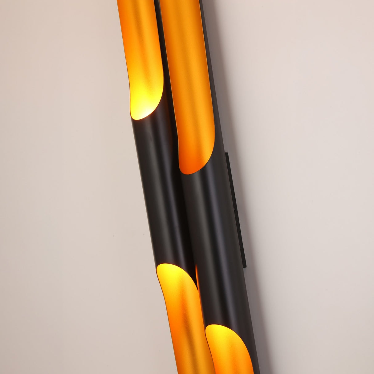 The Stealth 4 Light Wall Light in brass and black features a modern cylindrical design, blending black exteriors with warm glowing interiors, creating a bold statement on any light-colored wall.