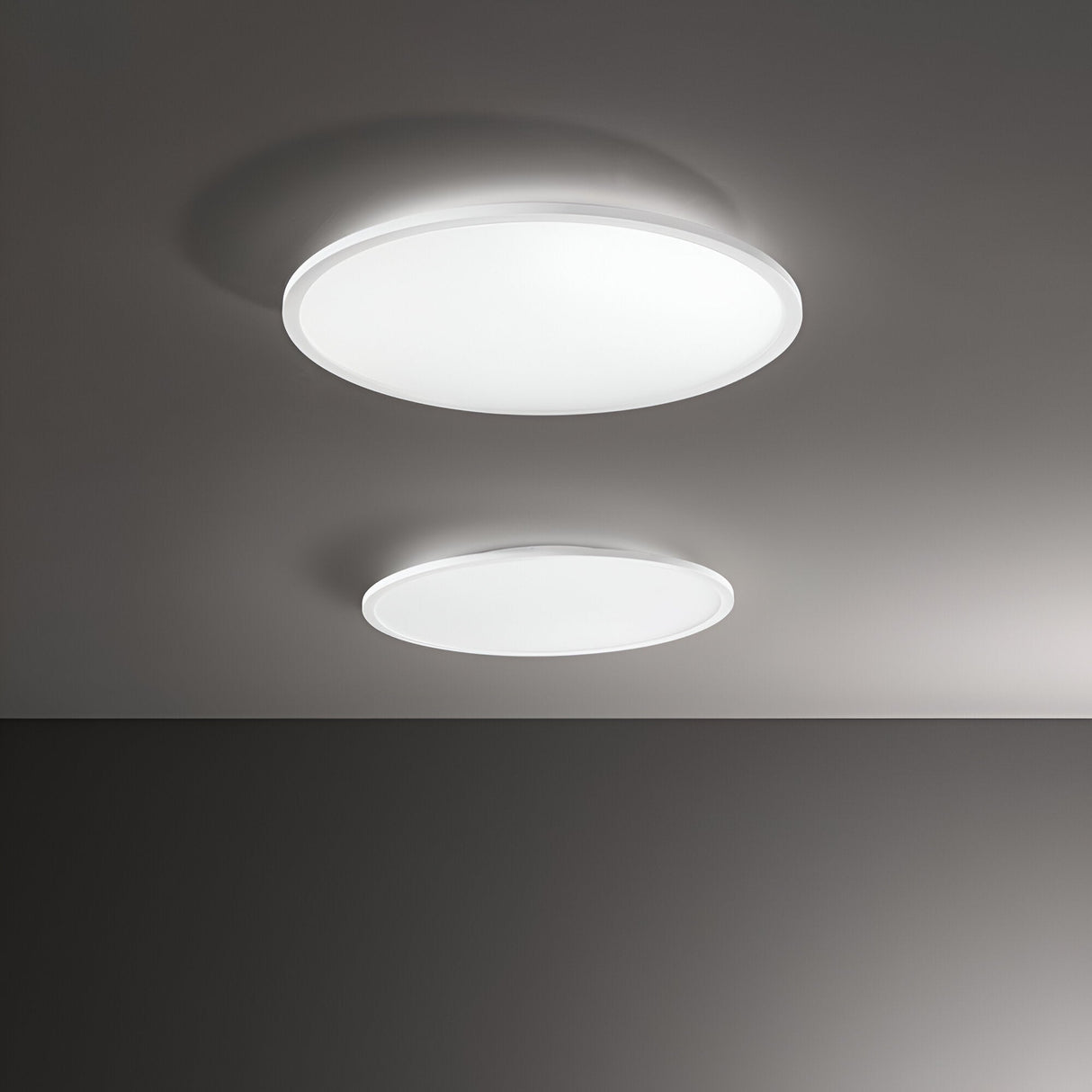 The image showcases two circular ceiling lights against a gray background. The Spark Slim LED Flush Lights, each emitting a soft white glow with energy efficiency, are turned on. This modern lighting solution features the larger Spark Slim LED Flush Light 53W 3000K - White, 60cm positioned above the smaller one.