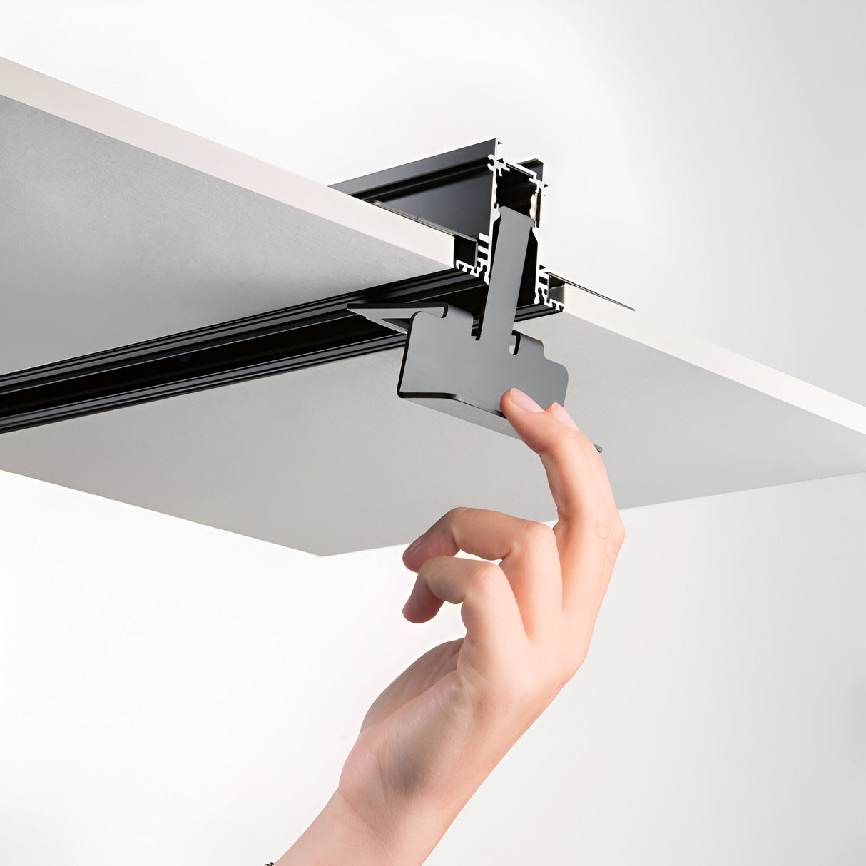 A hand adjusts a Luxeon Mounting Bracket for Track Lighting Systems in black, attached to a white panel, set against a plain background. The system seems designed for ceiling or wall installation, possibly featuring durable aluminium components for added reliability and ease.