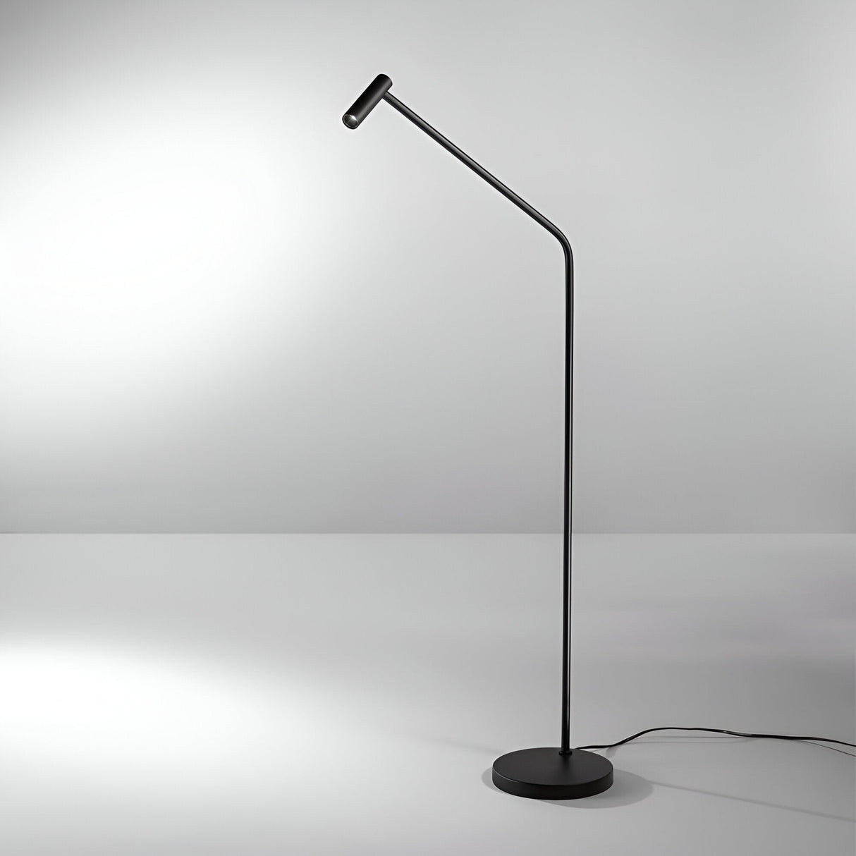 The Easy Floor LED Lamp - Black showcases modern simplicity with its sleek, angled design and round base, complemented by a light gray floor. Its soft light provides energy-efficient illumination, while a discreet black cord extends from the base.