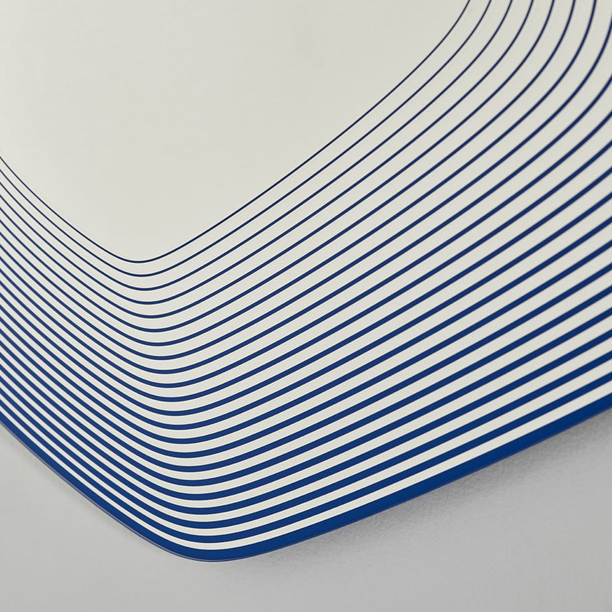 Close-up of the Vibe Blue Line Print Irregular Wall Mirror 80cm, showing concentric blue lines printed on glass, crowding tightly around a curved corner for a layered depth effect.