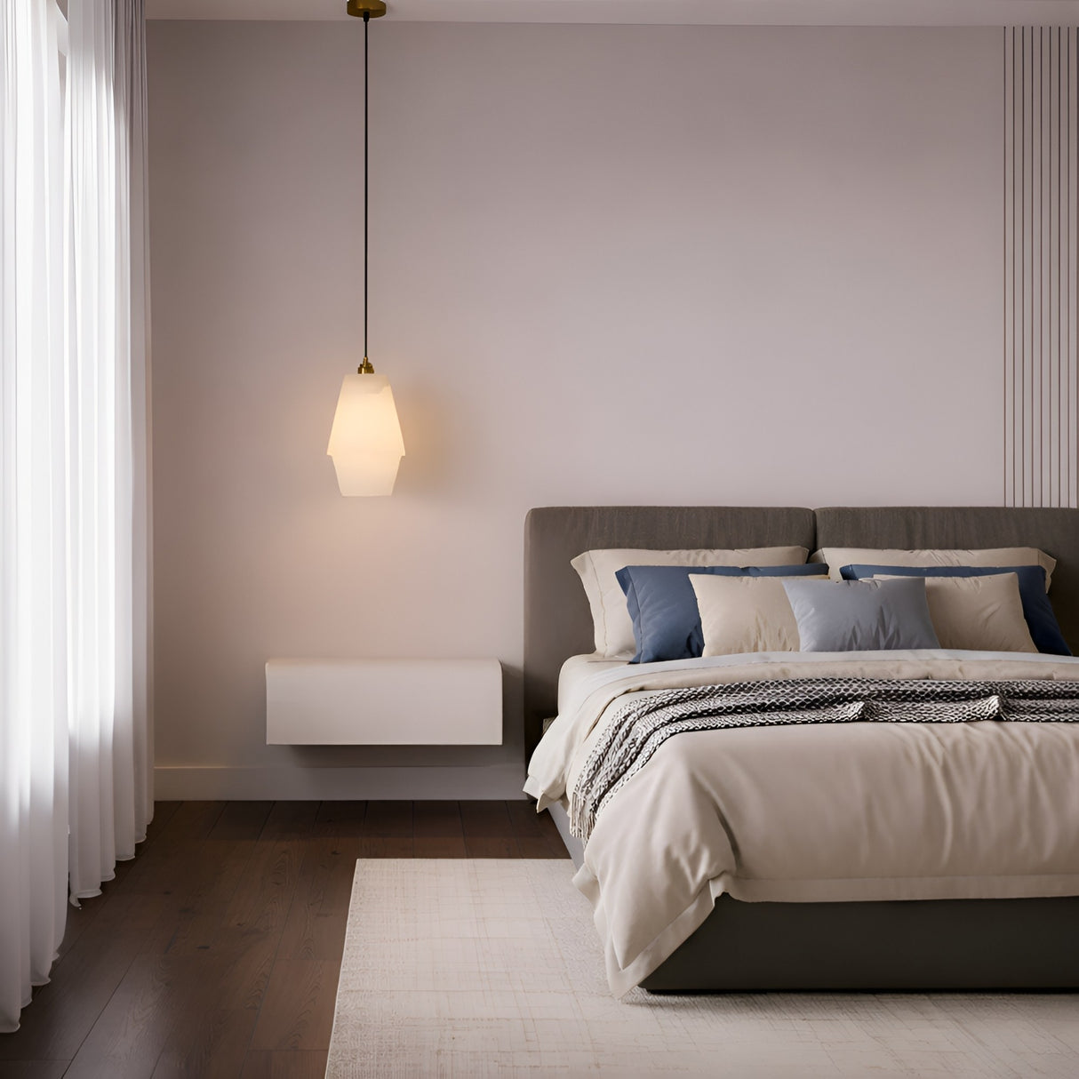 Minimalist bedroom with a neatly made bed featuring beige and blue pillows, a soft beige comforter, the Bellorin 1 Light Large Alabaster Single Pendant Light in Soft White & Brushed Brass, sheer white curtains, and dark wood flooring.