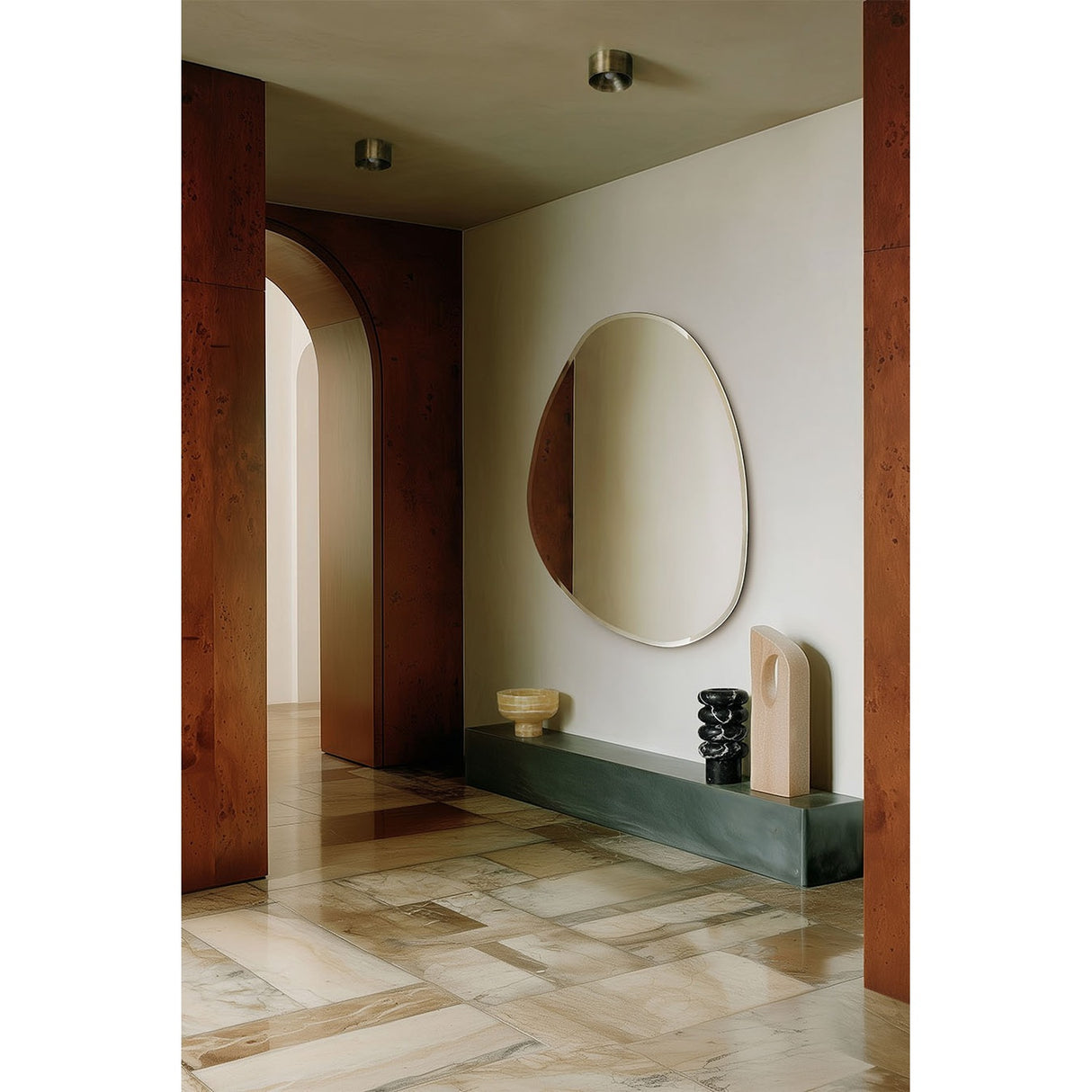 Pure Bevelled Edge Organic Wall Mirror 136cm, frameless irregular-shaped glass with bevelled edge, mounted on a wall above a dark console table in a hallway setting.