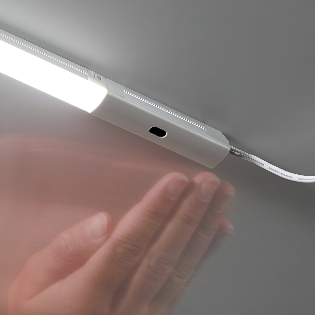 A person's hand hovers near the Nocturne Sensor Switch for Input Power Cord, activating a brightly lit LED light bar. The setup is mounted on a surface, showcasing seamless interaction with motion detection technology and a visible input power cord.