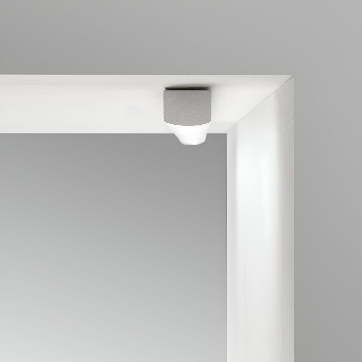 Close-up of a white rectangular frame featuring a small, gray cylindrical object at the corner, held in place by Nocturne Metal Mounting Clips with Screws. The background is a smooth, light gray surface, enhancing the image's minimalist appearance.