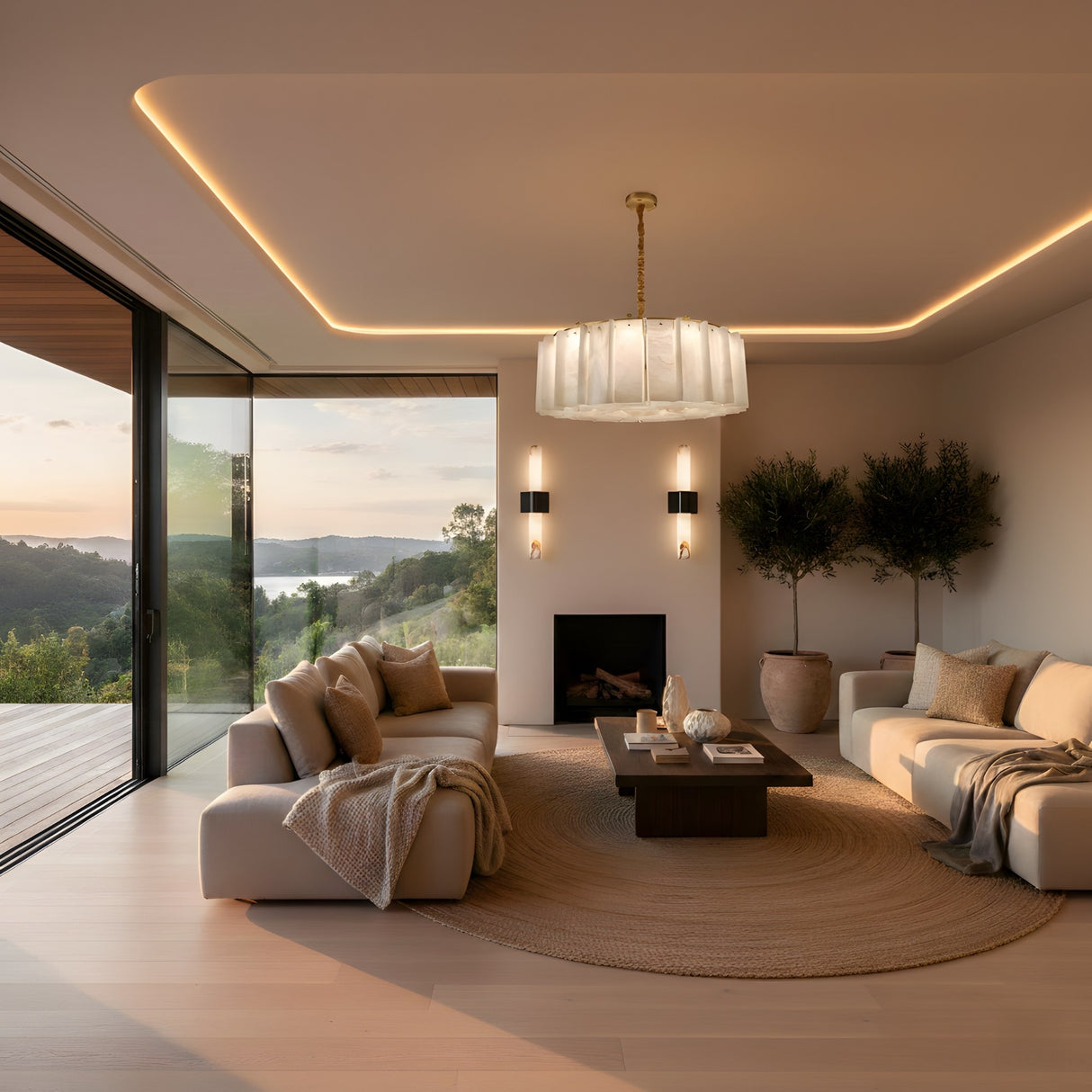 A modern living room with neutral sofas, a round rug, potted trees, a wooden coffee table, and the Lunaro 12 Light Circular Panel Alabaster Chandelier in brushed brass & soft white. Sliding glass doors showcase a sunset as warm lighting sets a cozy mood.