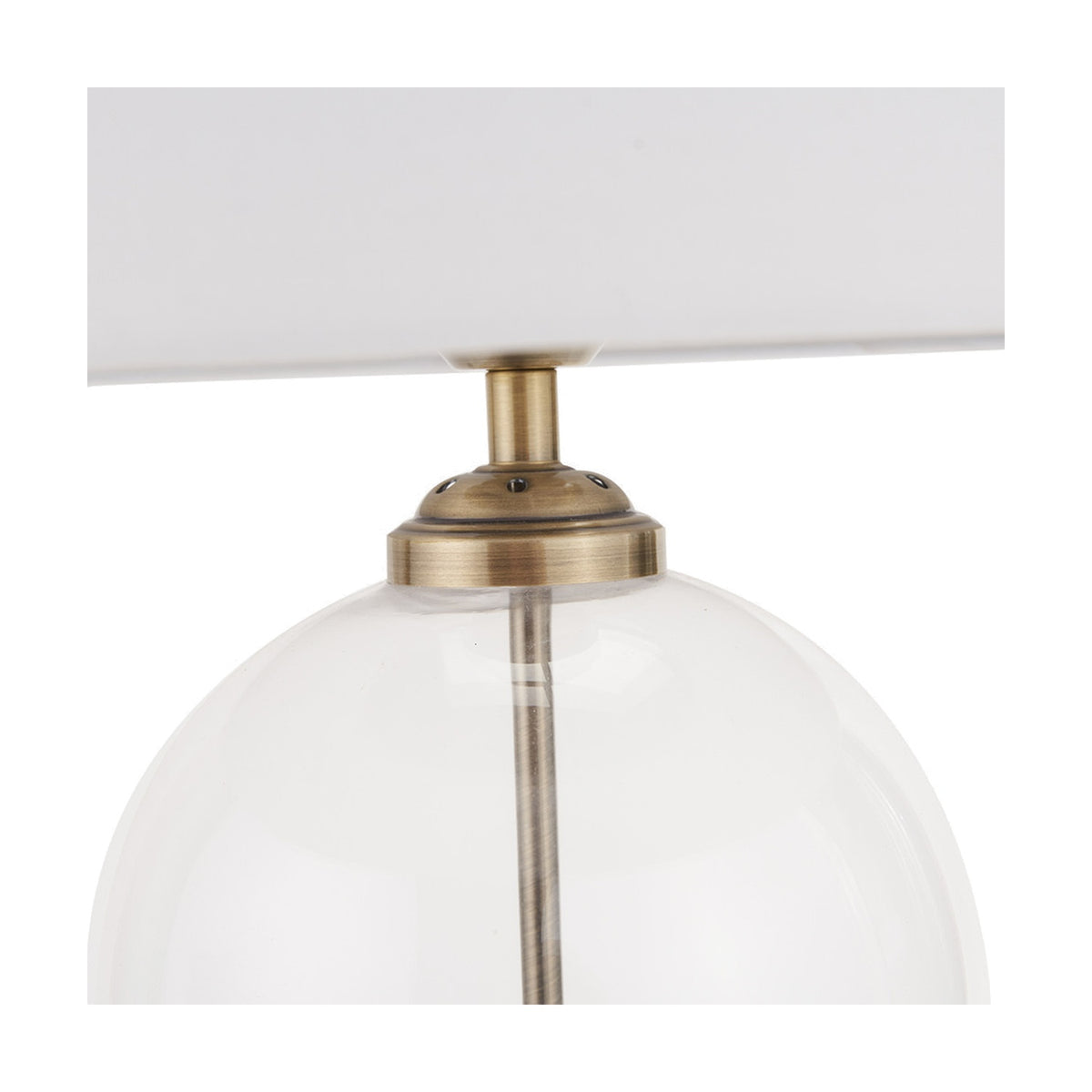 Close-up of the Cloche table lamp's antique brass fitting atop a clear glass globe base, with white fabric shade, against a plain white background.