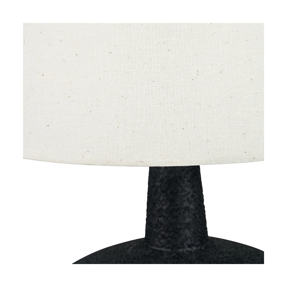 Close-up of the Elio table lamp's textured black ceramic base and neck beneath a white linen drum shade, shown against a plain background.