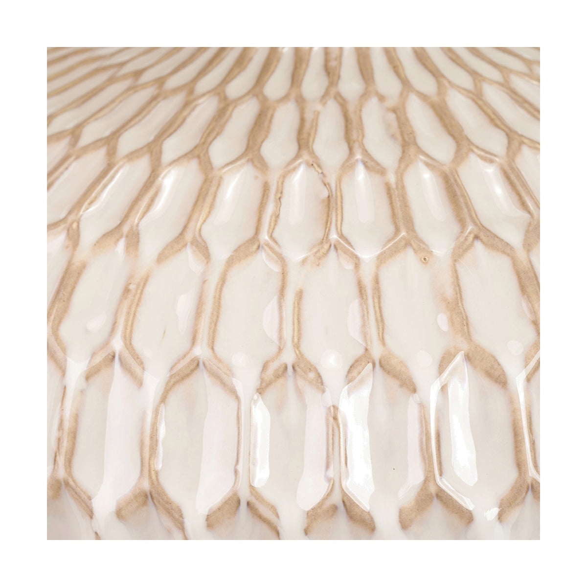 Close-up of the Cassius table lamp's ceramic base showing a raised honeycomb texture in warm white with tan-toned glazed grooves catching the light.