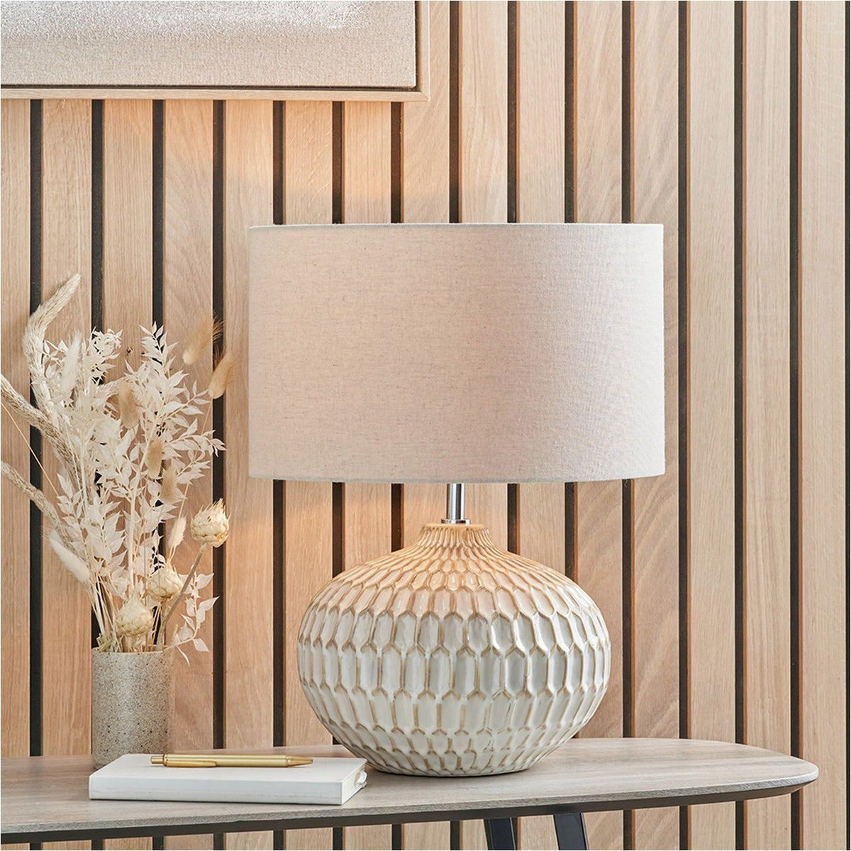 Cassius Warm White Textured Glazed Ceramic Table Lamp, 48cm, with honeycomb-textured base and linen drum shade, styled on a console table beside dried florals and a wood-slat wall.