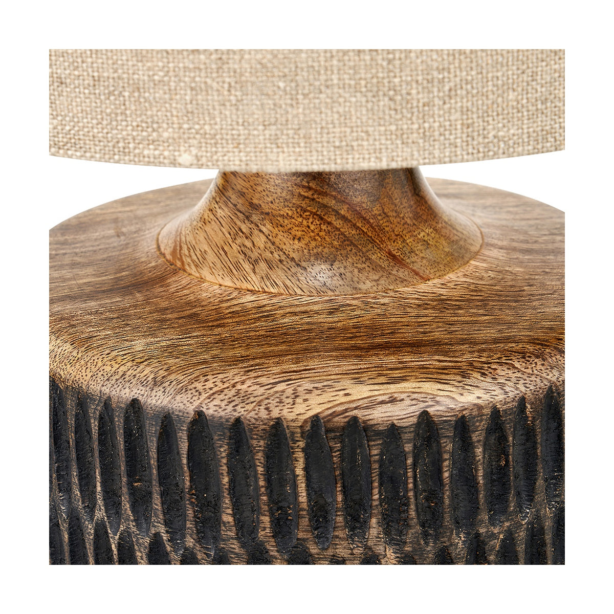 Close-up of the Alaric table lamp base in antique black wash mango wood, showing carved textured lower band, natural grain, and a linen shade edge above.