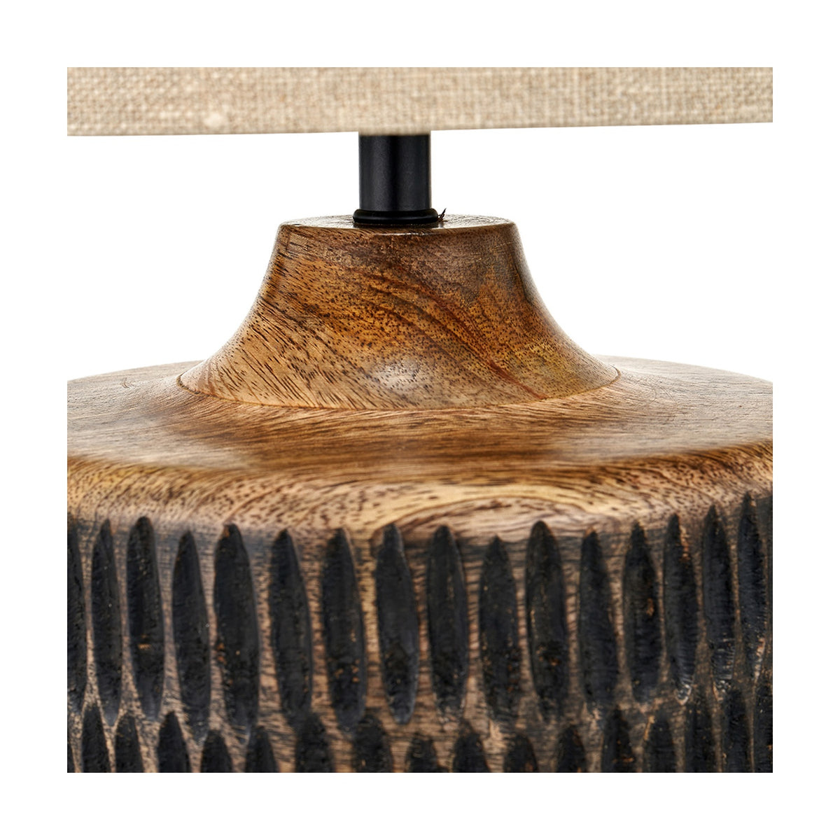 Close-up of the Alaric table lamp's mango wood base with carved vertical fluting in antique black wash, tapering neck, and black metal fitting beneath a linen shade.
