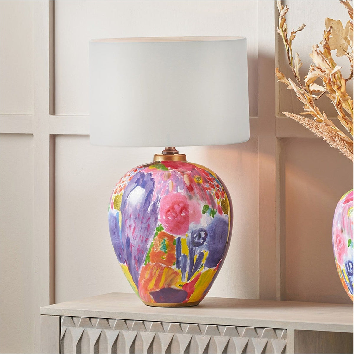Matisse Multi Colour Ceramic Urn Table Lamp Base, 42cm, with a white drum shade, shown lit on a wooden console in a living room setting.