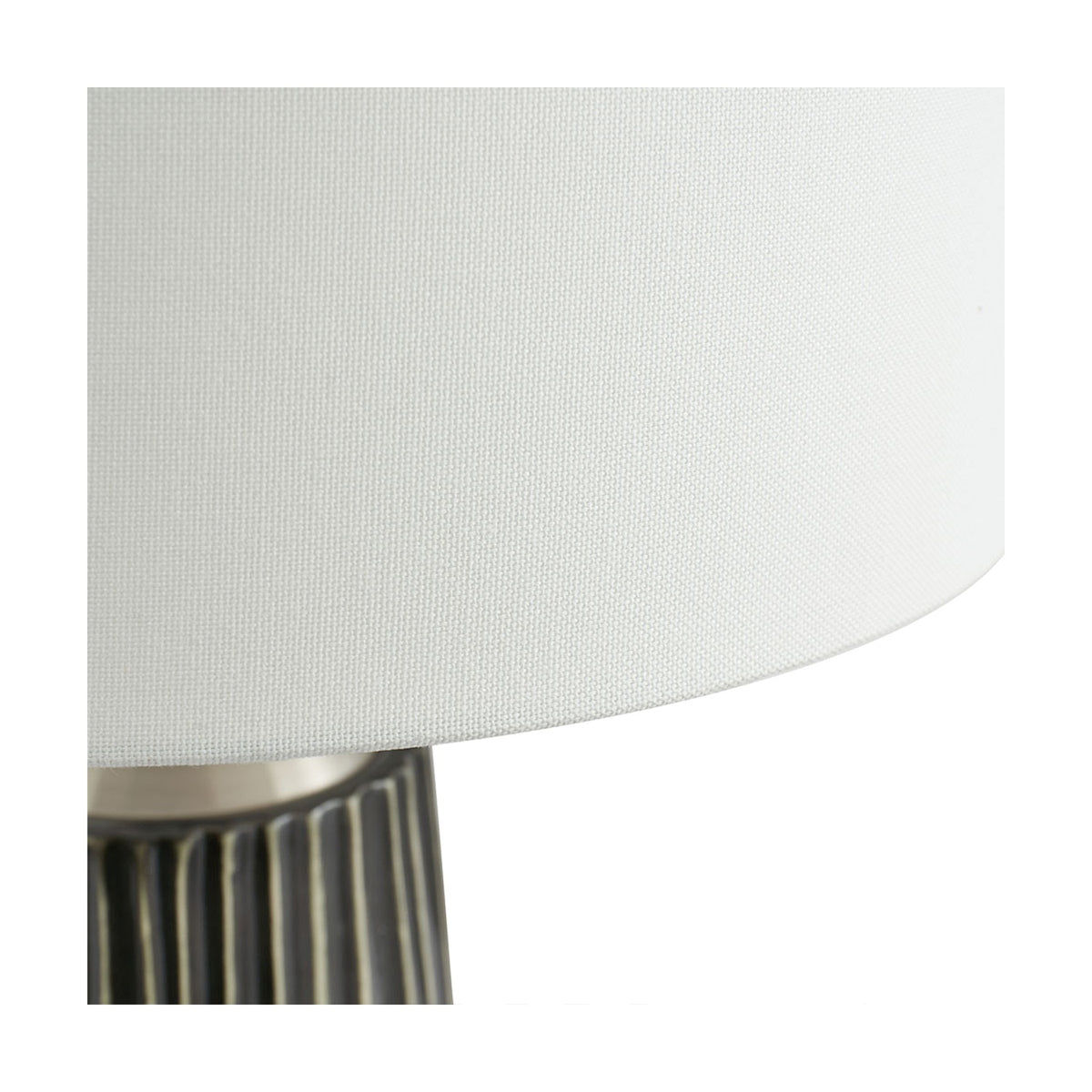 Close-up of the Artemis table lamp's white fabric drum shade meeting its black ridged ceramic base with brushed silver trim.