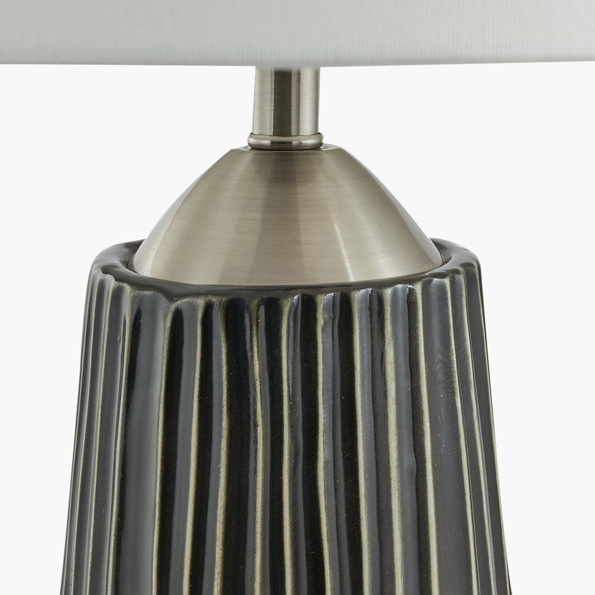 Close-up of the Artemis table lamp base, showing black ridged ceramic body with brushed silver cone fitting and neck below a white fabric shade.