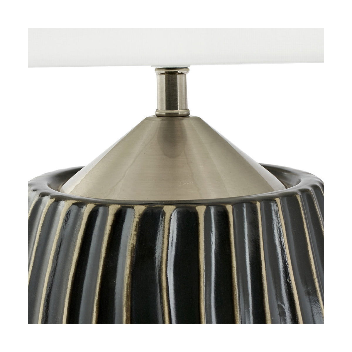 Close-up of the Artemis table lamp's ribbed black ceramic base with brushed silver cone connector beneath a white fabric shade, on a plain background.