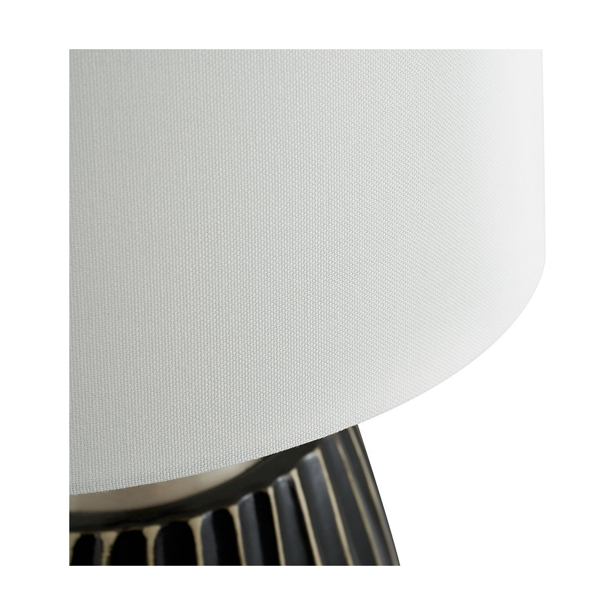 Close-up of the Artemis table lamp showing the white fabric drum shade edge above a black textured ceramic base with fluted ribbing.