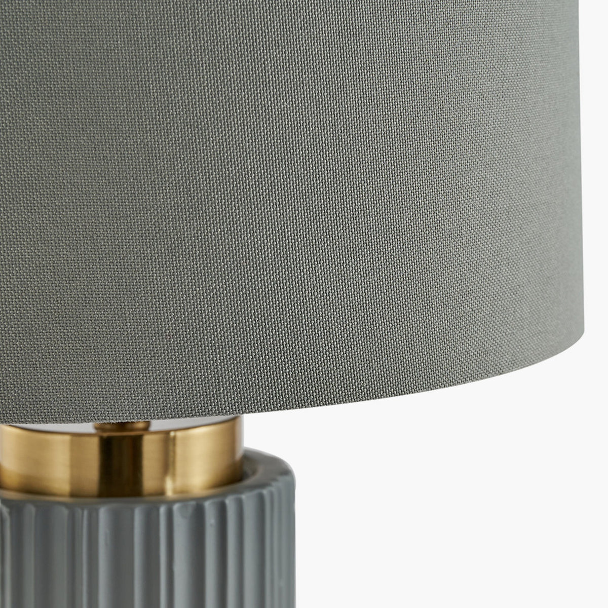Close-up of the Ionic Grey Textured Ceramic & Gold Metal Table Lamp, showing the ribbed grey ceramic base, brass connector ring, and grey fabric drum shade.