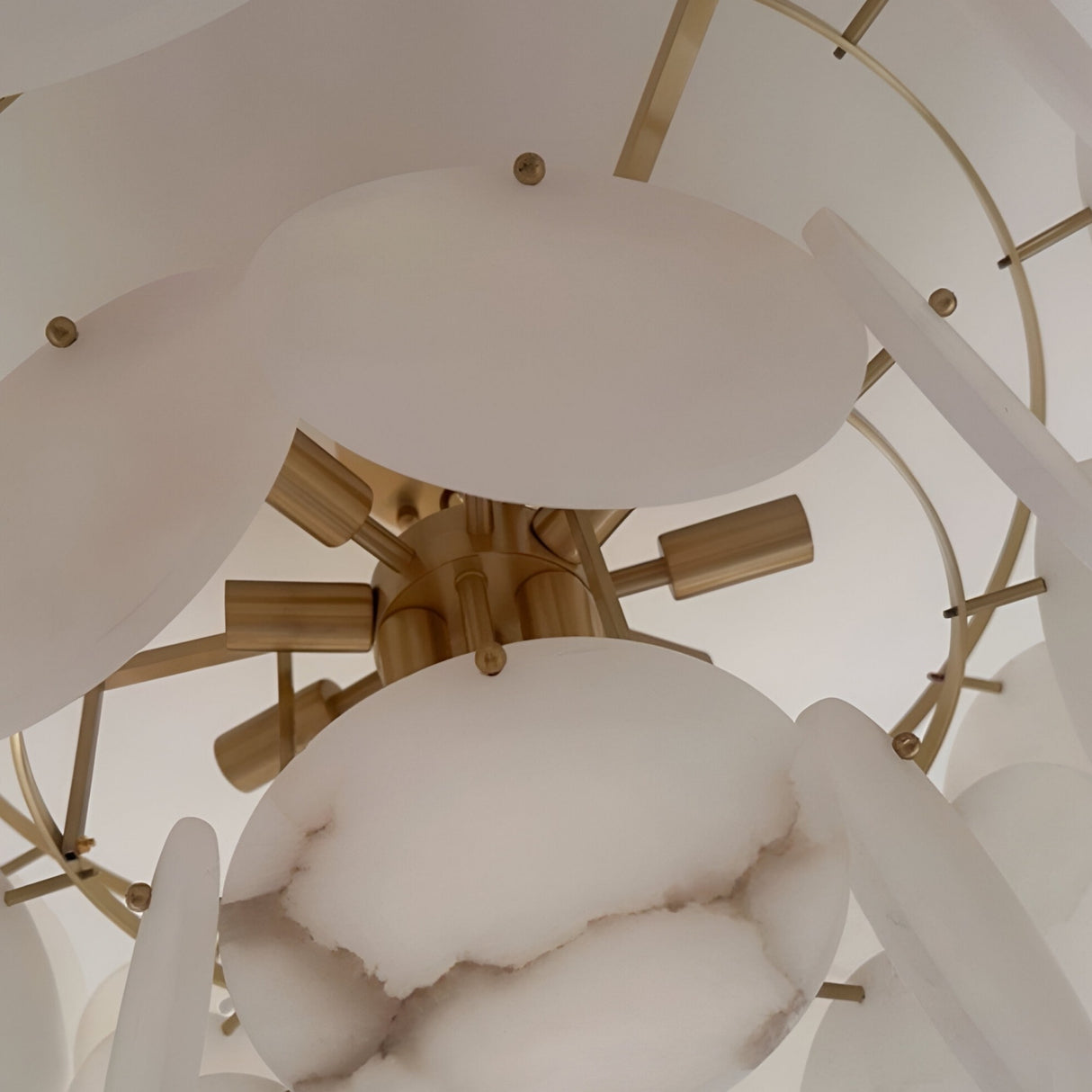 Close-up of the Solyra 6 Light 2 Tier Petal Alabaster Chandelier in Soft White, featuring round alabaster discs and gold rods arranged in a modern, layered pattern against a neutral backdrop.