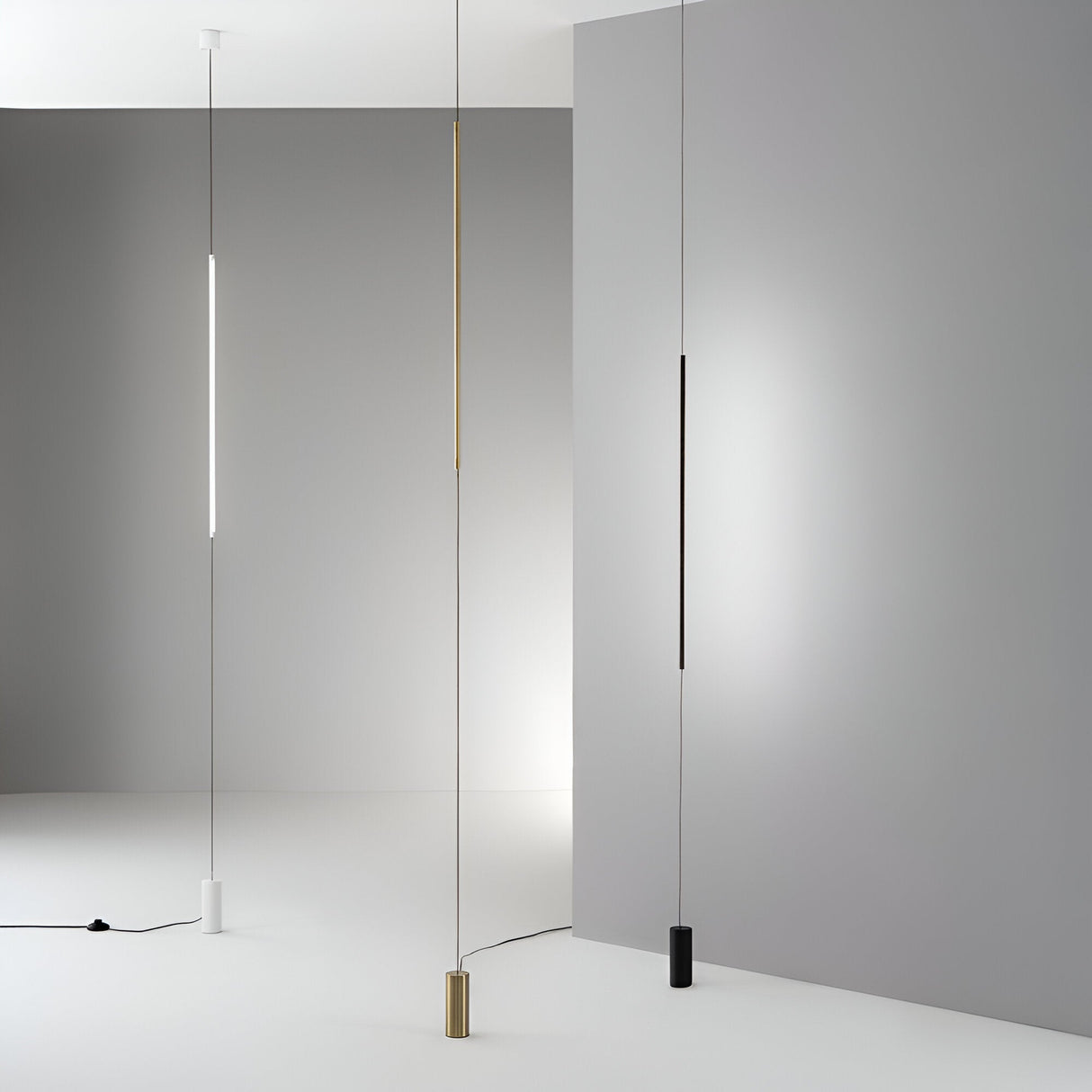 The minimalist room showcases the Celestia LED Floor Lamp in white, complemented by three slender pendant lights in white, gold, and black finishes. These energy-efficient LED lights elegantly hang from the ceiling against a gray wall, creating a stunning contrast with the white floor and background.
