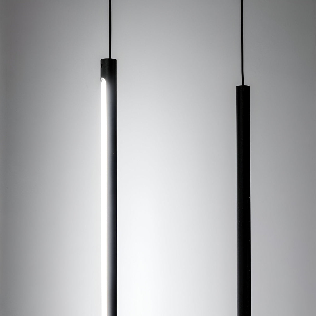 Two sleek, cylindrical Celestia LED Floor Lamps - Black are arranged against a plain gray background. The left lamp is illuminated, emitting a soft glow that highlights the charm of modern lighting, while the right lamp remains unlit. Both lamps boast a minimalist design and feature thin black cords for hanging.