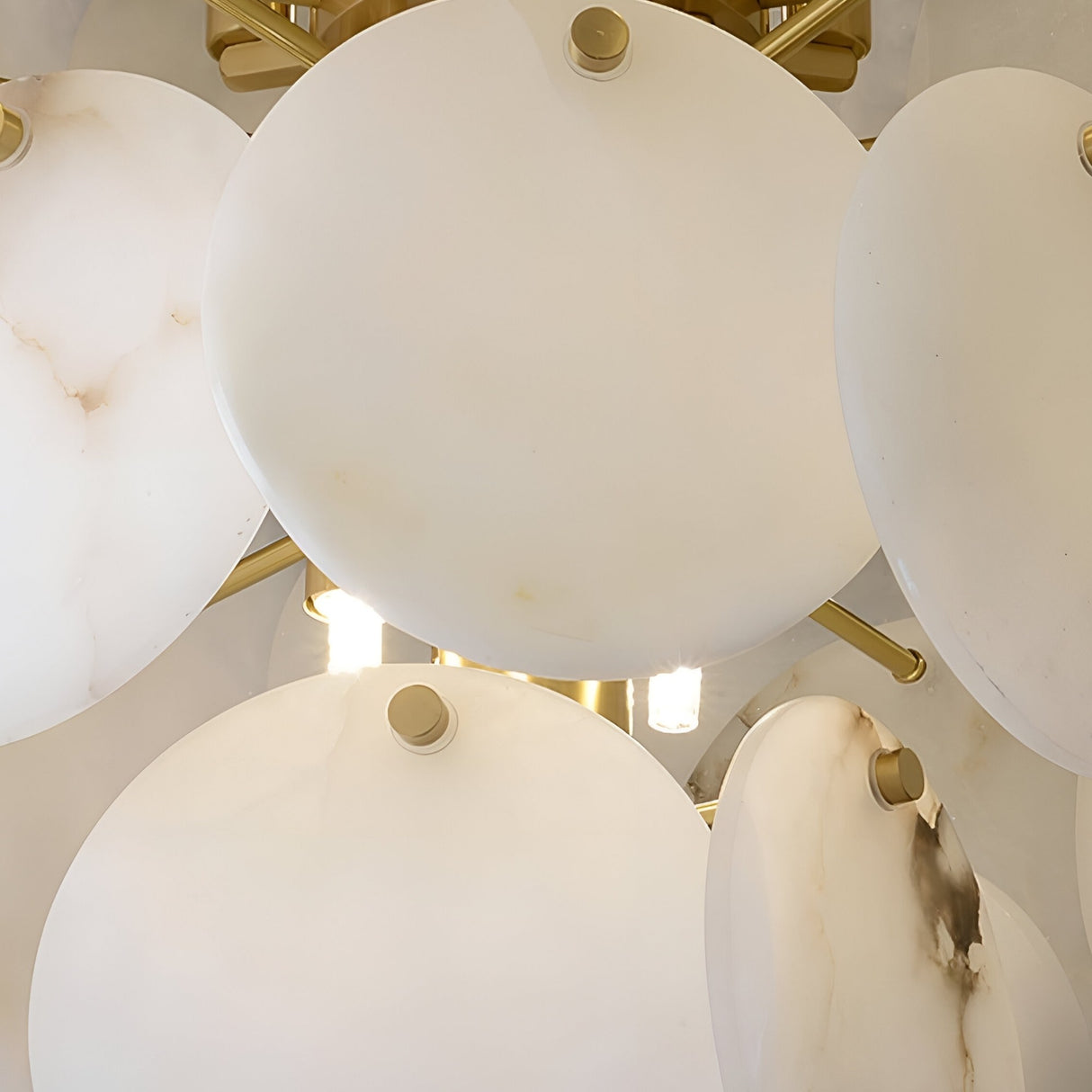 Close-up of the Solyra 6 Light 2 Tier Petal Alabaster Chandelier in Soft White, featuring large round alabaster discs and gold accents, partially concealing multiple bright bulbs behind them.