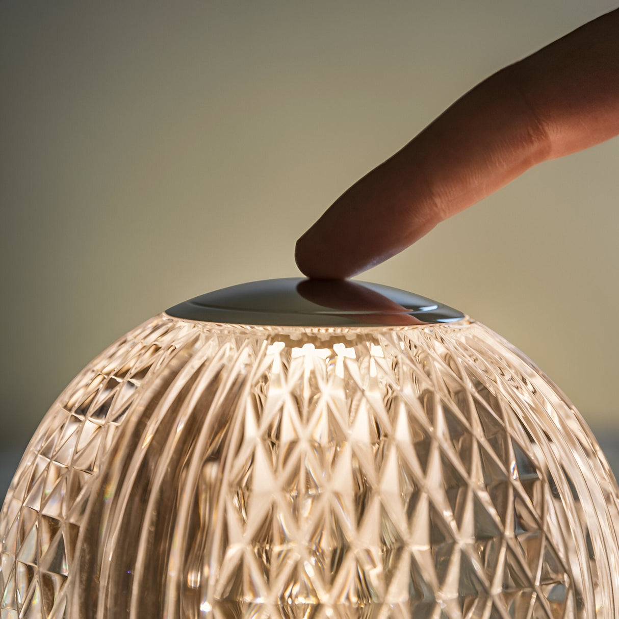 A finger touches the top of the Lustris LED Table Lamp 2.2W 3000K - Clear, featuring a geometric pattern and textured glass, creating a warm glow.