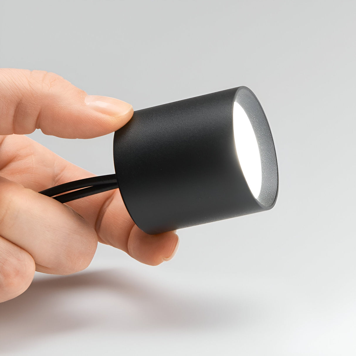 A hand holds the Solace LED Round Downlight 4W 4000K in a sleek, black design with wires extending from the back. The light is turned on, emitting a bright white glow that complements modern lighting solutions. The background is neutral.