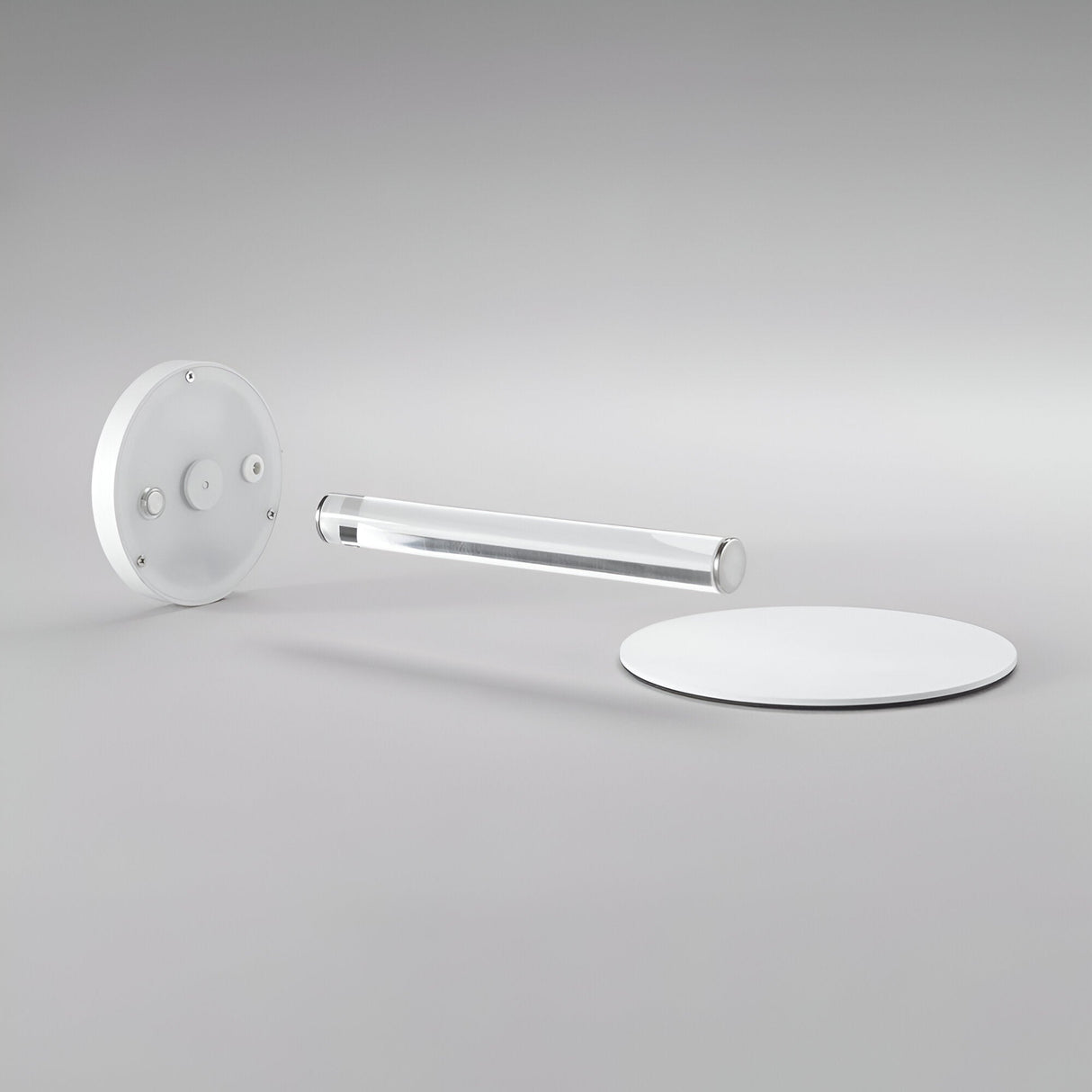Minimalist photo featuring the contemporary design of the Solixis LED Table Lamp 3.6W 3000K - White: it includes three geometric elements—a circular white base, a clear cylindrical rod at its core, and a round white disc in the background—all arranged on a light gray surface. Ideal for battery-operated elegance.