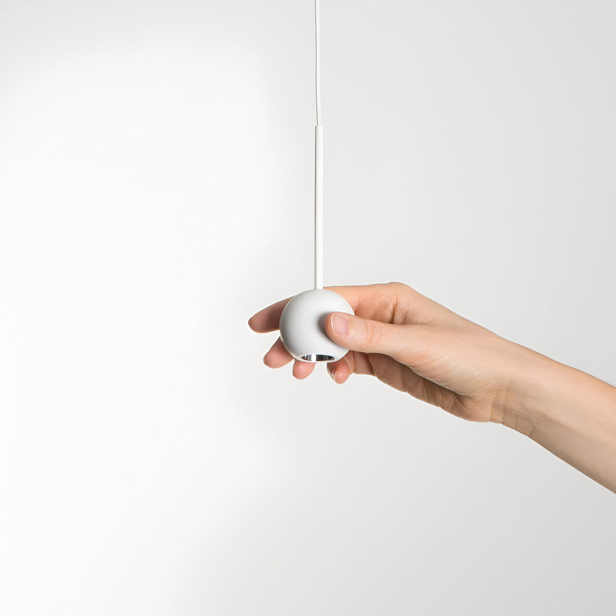 A hand adjusts the height of the Arclight LED 1 Light Sphere Pendant - White, elegantly suspended from the ceiling by a thin cord. The spherical design seamlessly integrates with modern interiors, casting efficient lighting against a plain white background.