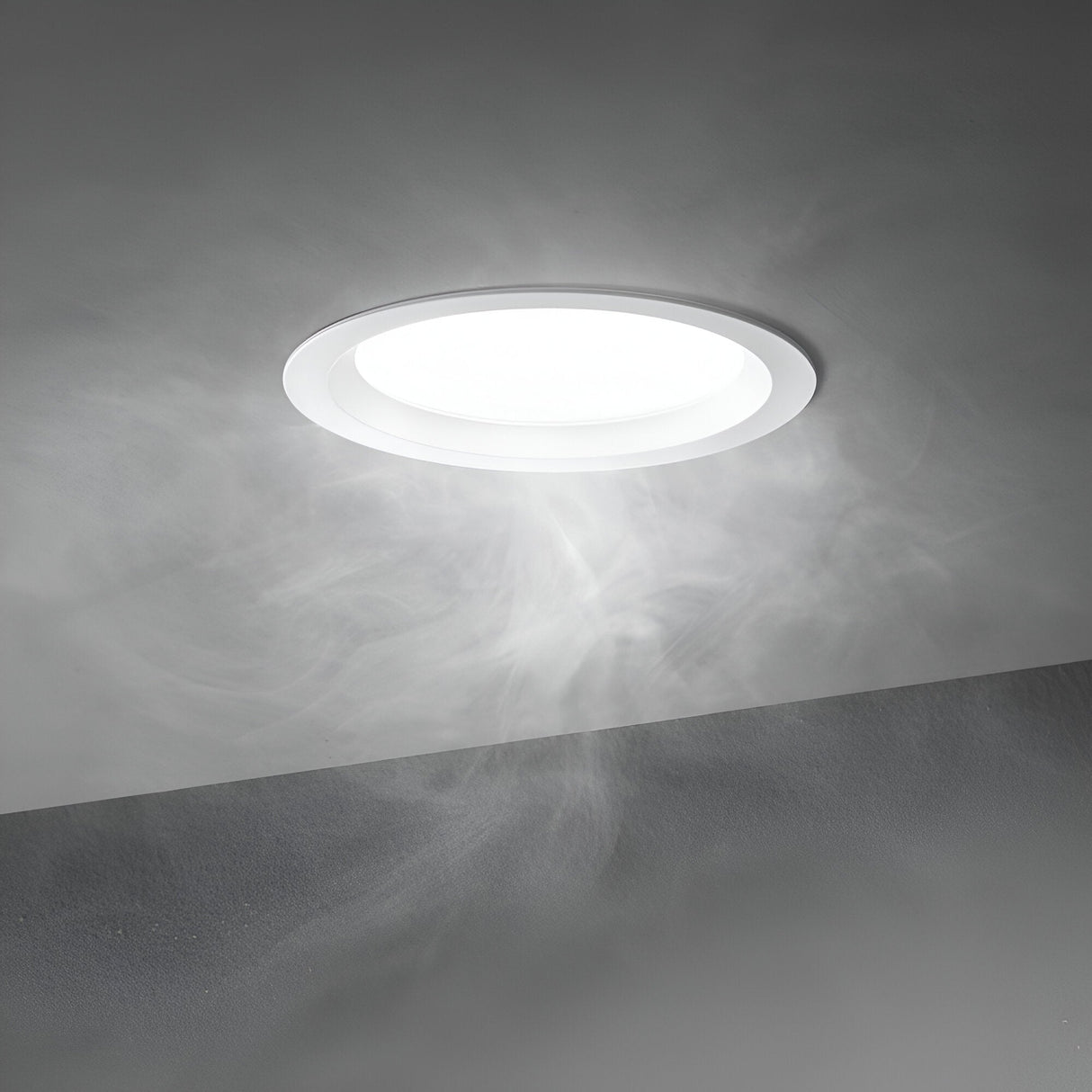 The Radiara-2 Round LED Recessed Downlight, boasting an IP65 protection rating, peers through the swirling mist, casting a soft glow on the grey ceiling and wall. It embodies both energy-efficient lighting and modern elegance with its 46mm size, 20W power, warm 3000K color temperature, and sleek white finish.