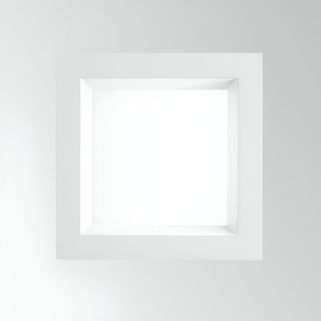 The Radiara-2 Square LED Recessed Downlight 215mm - 25W, in a clean white finish, features a geometric square design with a beveled border that casts subtle shadows against its light gray backdrop. Its minimalist form is reminiscent of an LED bulb glowing at 3000K, highlighting symmetry and depth.