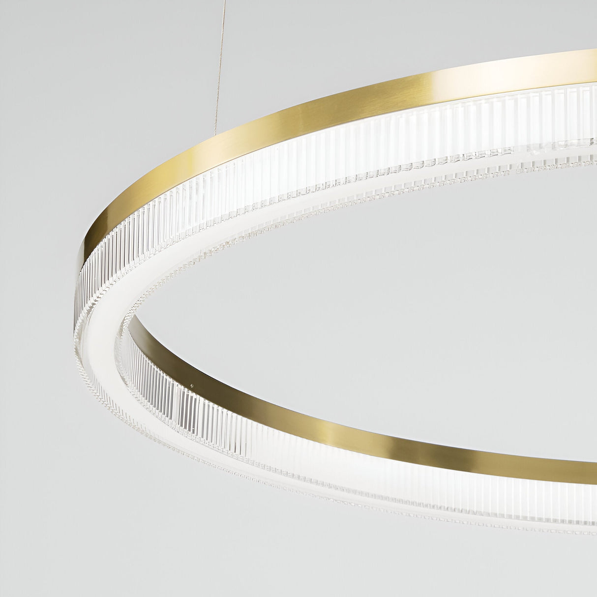 A close-up of the Soltra LED Light Suspension 30W 3000K - Brass, 80cm, a modern circular ceiling light fixture featuring a brushed brass rim and clear ribbed acrylic detailing. This sleek and elegant design is highlighted by an opal acrylic diffuser against a plain white background.