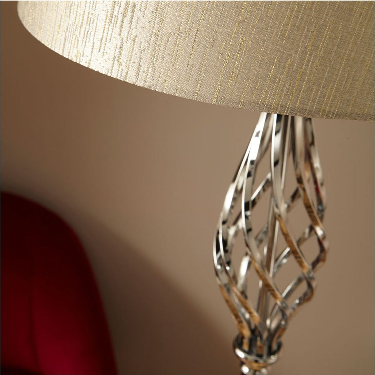 Close-up of the Jenna Silver Metal Twist Detail Floor Lamp, showing the spiral chrome-finish stem and neutral fabric shade above a red chair.