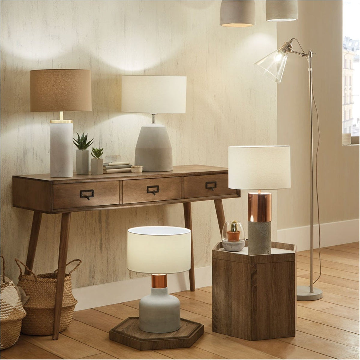 Chaplin Floor Lamp in brushed chrome with an angled glass shade and concrete base, shown in a living room beside a wooden console table and table lamps.