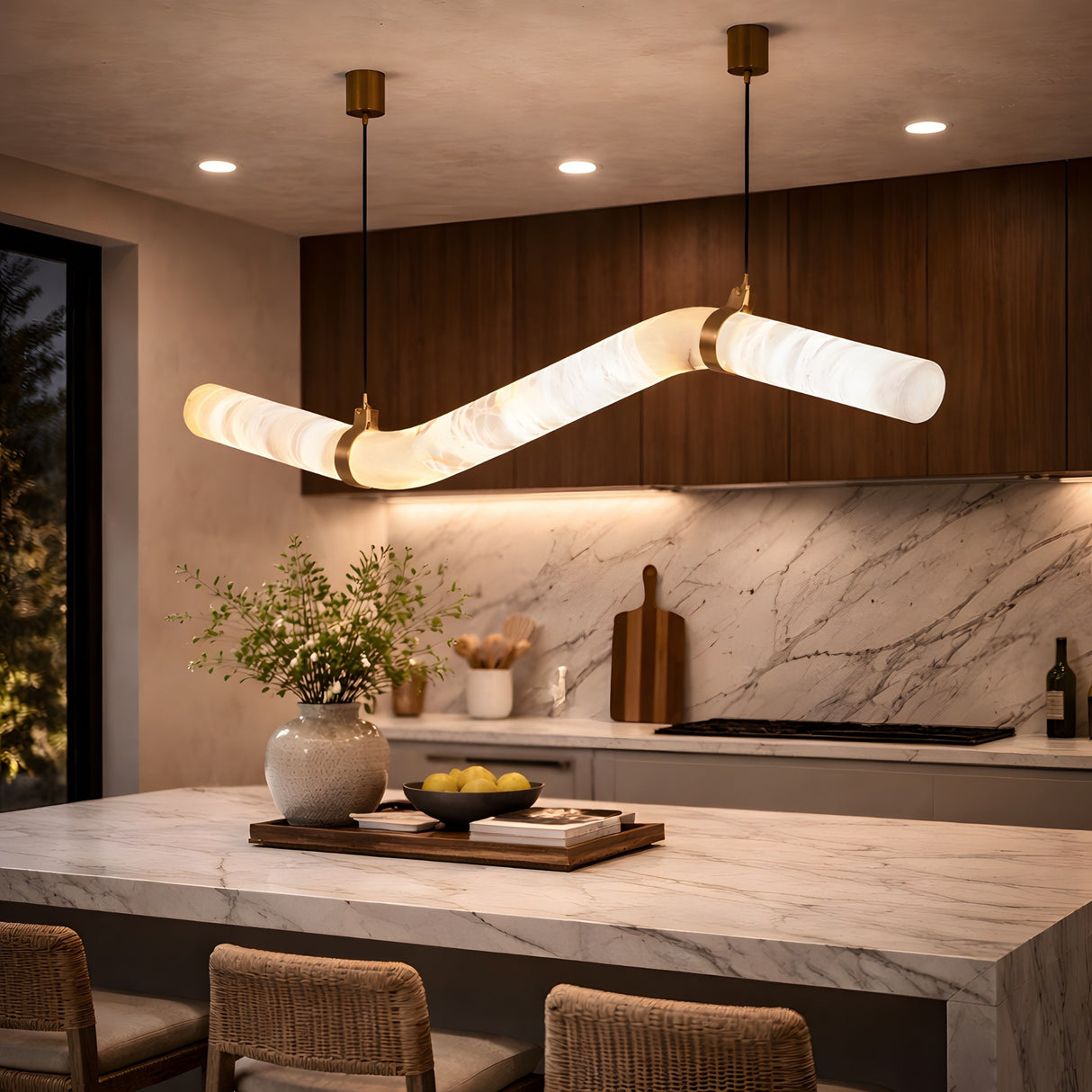 Modern kitchen with marble countertops, wooden cabinets, and the Zareon LED Medium Articulated Alabaster Suspension Light in Soft White. A vase of greenery and lemons decorate the island, with woven stools tucked underneath.
