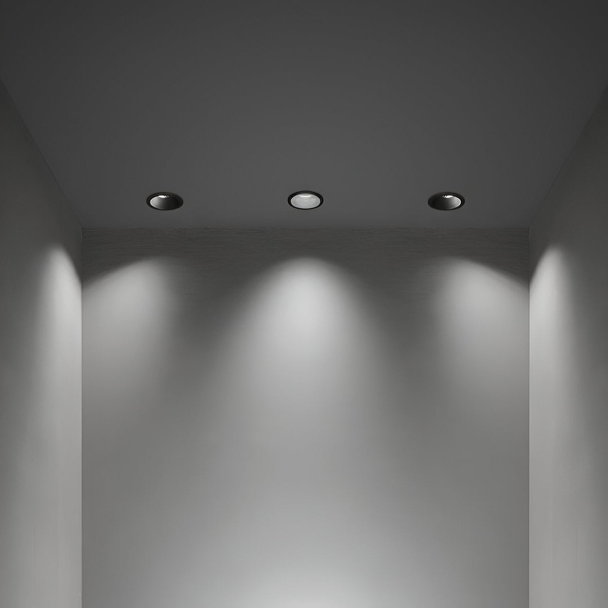 A minimalist room with modern lighting installation features three recessed ceiling lights that illuminate the gray walls with soft, overlapping circles of light. The Glistenis Trim Round Frame For Downlight 77mm - Black enhances the clean and modern atmosphere of the space.