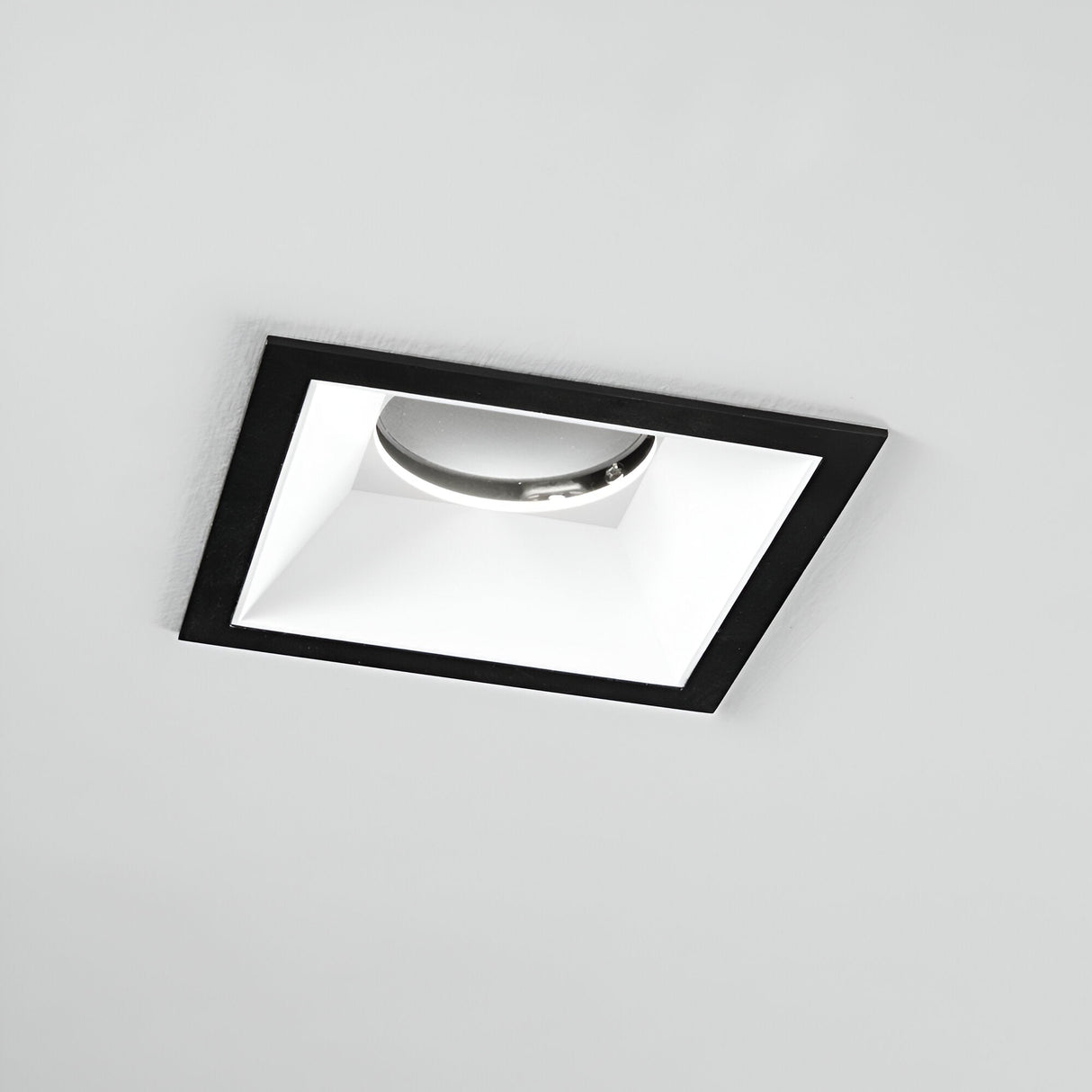 The Glistenis Trim Square Frame 106mm in black offers a modern, recessed ceiling light design with a sleek finish and reflective interior. Shown turned off against a plain white ceiling, it exemplifies the elegance of contemporary downlight installations.