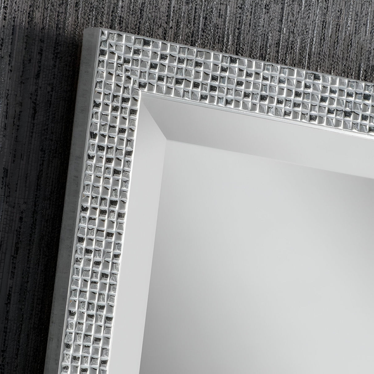 The Frost Rectangle Wall Mirror - Silver features a close-up view highlighting its superior craftsmanship with a textured, reflective grid pattern. Set against a dark, textured wall backdrop, the mirror's gleaming silver frame exudes modern luxury through its rectangular form.